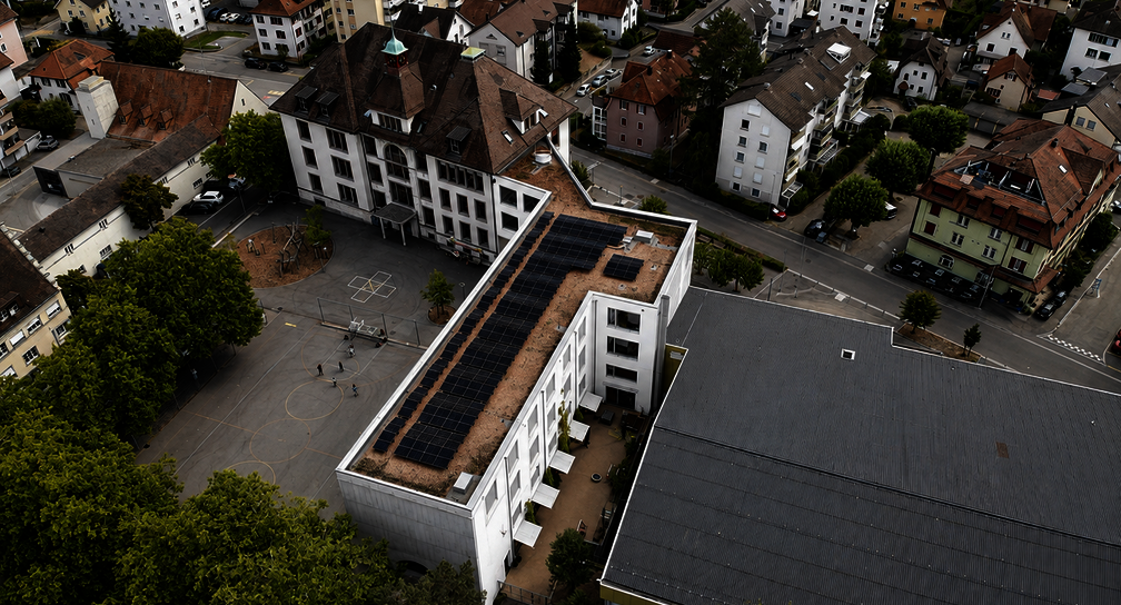 Dachansicht der 54-kWp-Solaranlage auf dem Schulhaus Kirchacker in Neuhausen am Rheinfall mit Schulhof und bestehender Schulinfrastruktur.